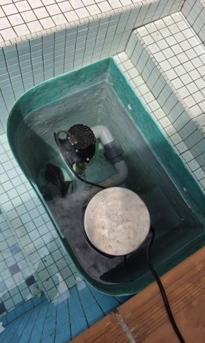 Close-up of internal PVC pipe fittings and electric pump inside a teal plug and play pool filter box.