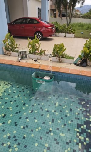 Teal plug and play pool filter box mounted inside a tiled swimming pool next to its external control box.