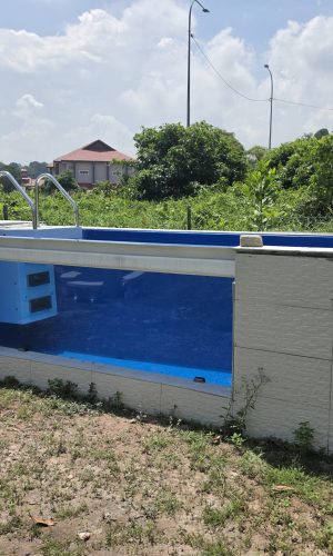 Exterior front-facing view of a custom glass-window swimming pool featuring an internal blue plug and play filtration system.