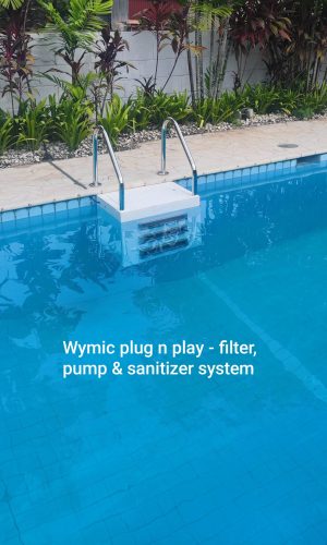 Wymic plug and play pool filter, pump, and sanitizer system mounted in a blue tiled outdoor swimming pool with stainless steel handrails.