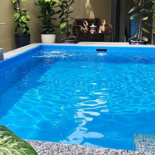 A bright blue residential backyard pool showcasing a smooth, leak-proof FRP laminate surface and a stainless steel water feature.