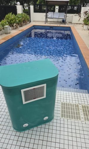 Standalone teal plug and play pool filter casing placed on white deck tiles next to a residential swimming pool.